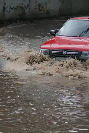 Um carro vermelho a passar no meio de uma estrada inundada